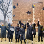 Photo of college graduates in their graduation gowns throwing their caps in the air.