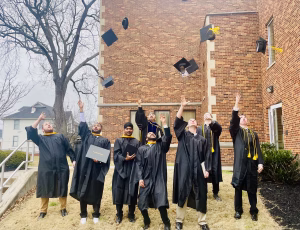 Photo of college graduates in their graduation gowns throwing their caps in the air.