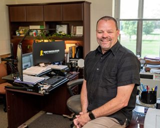 picture of Michael Casey seated on desk in his office, program coordinator