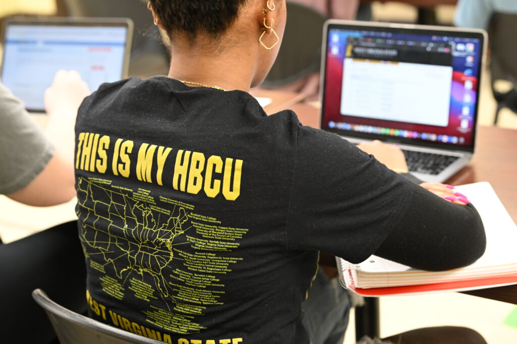 Student sitting at a laptop with a black t-shirt that says "This is my HBCU"