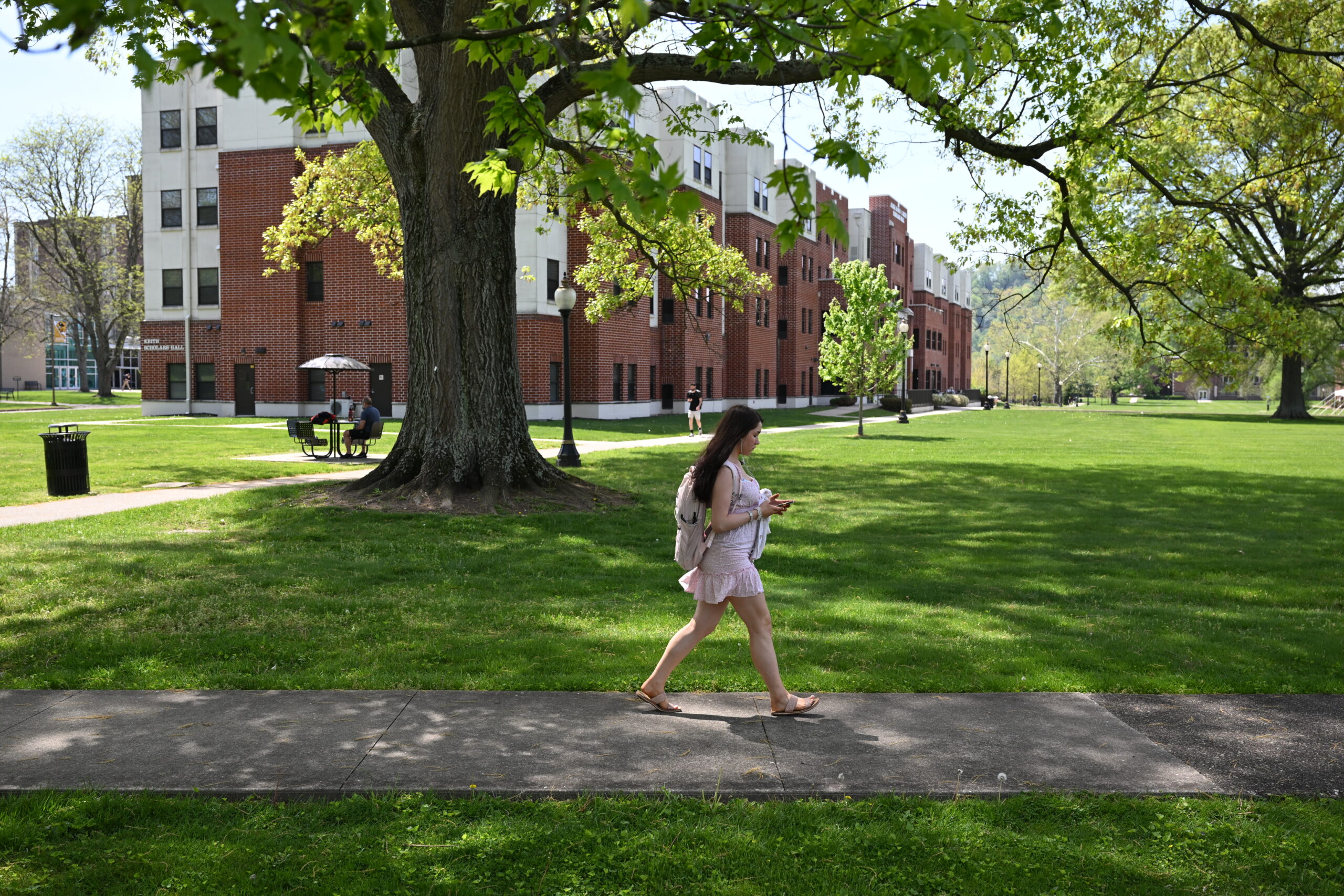 A female college student walks across the WVSU campus under trees 